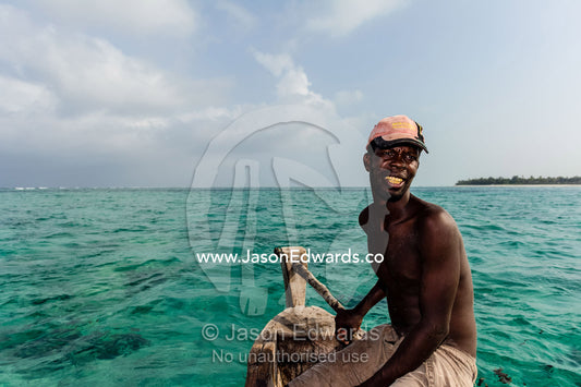 A fisherman steers his wooden trimaran sailing dhow in the shallow Indian Ocean. Bwejuu, Unguja Island, Zanzibar, Tanzania, Africa.