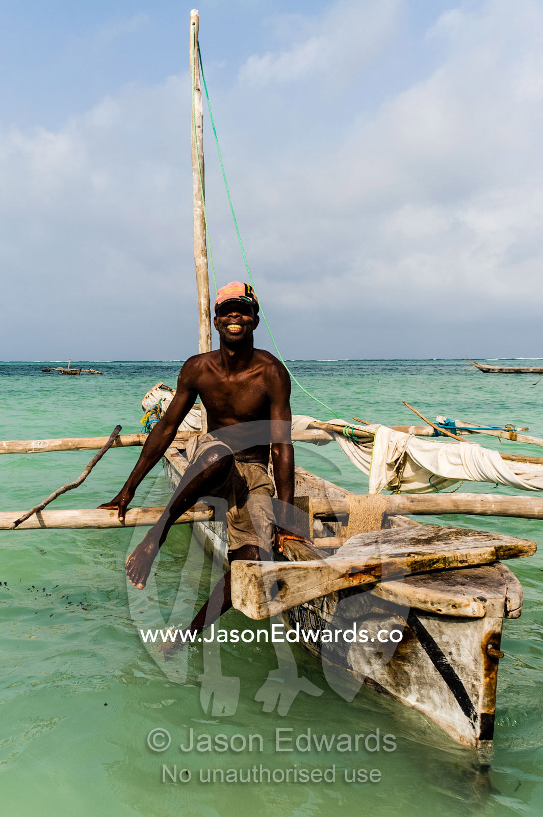 A fisherman moors his wooden trimaran sailing dhow in the shallows at sunset. Bwejuu, Unguja Island, Zanzibar, Tanzania, Africa.