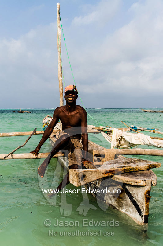 A fisherman moors his wooden trimaran sailing dhow in the shallows at sunset. Bwejuu, Unguja Island, Zanzibar, Tanzania, Africa.