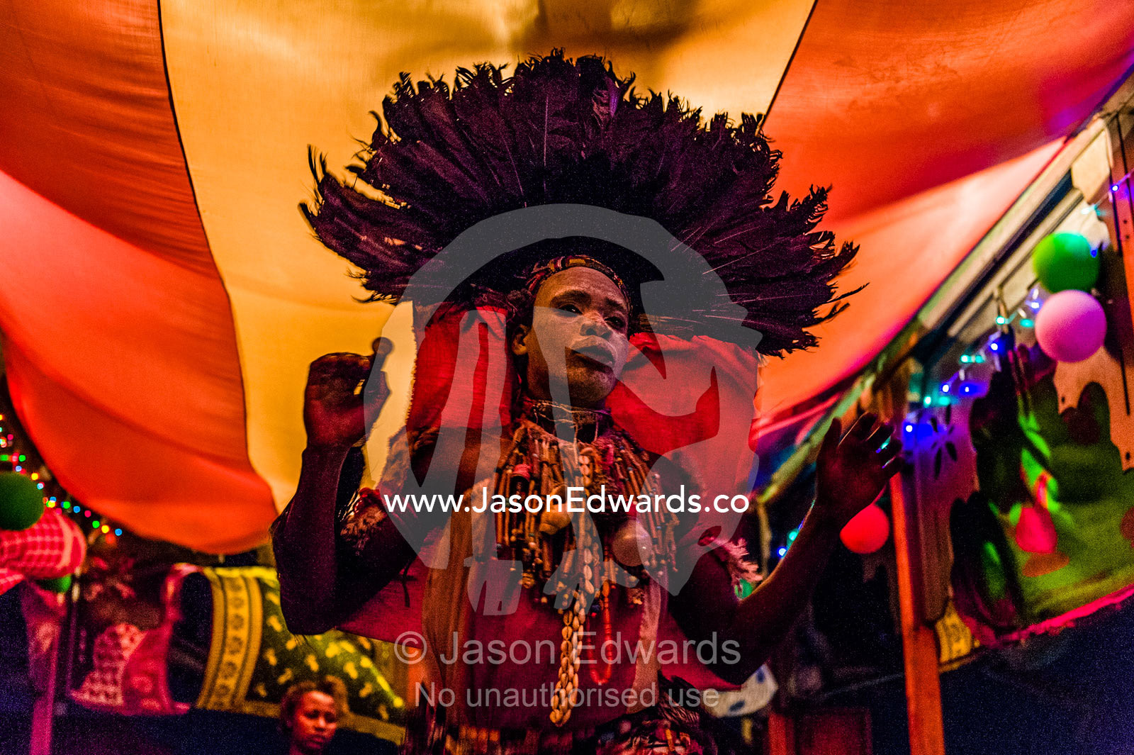 A spirit dancer decorated in facial paint, shells, beads and a feathered headdress performing at a rooftop restaurant at night. Stone Town, Mji Mkongwe, Zanzibar, Unguja Island, Zanzibar, Tanzania.