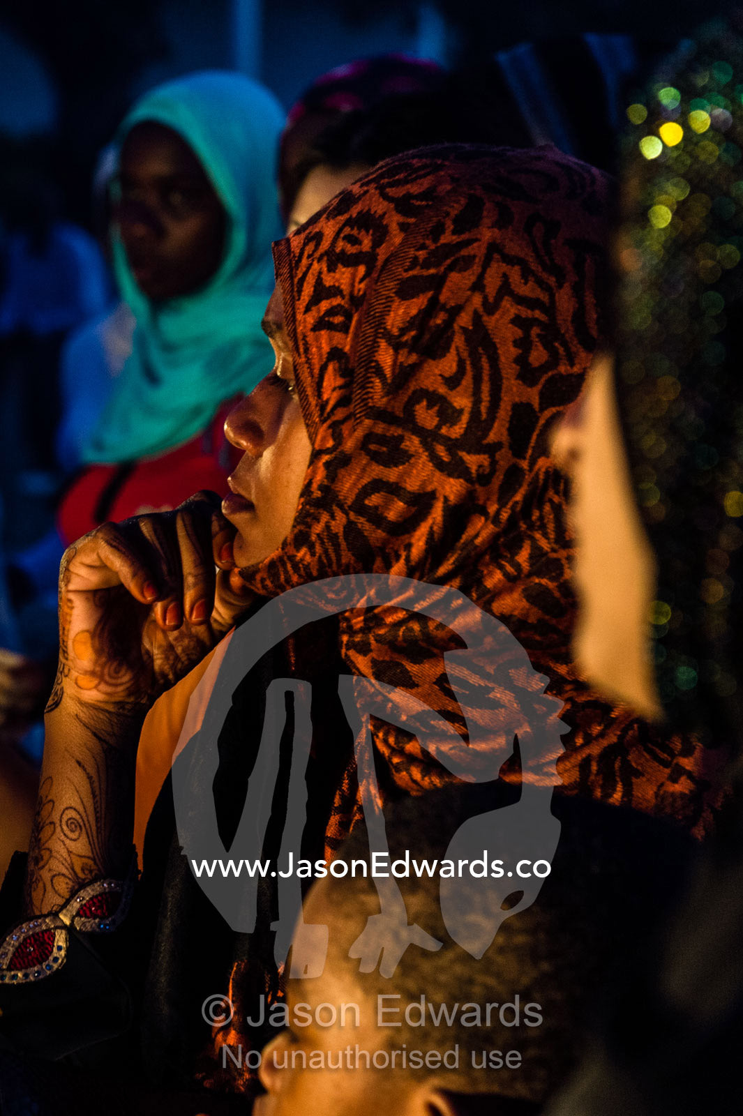A Muslim woman with henna tattoos waits to be served at a food stall in a crowded night market. Forodhani Gardens, Stone Town, Mji Mkongwe, Zanzibar, Unguja Island, Zanzibar, Tanzania.