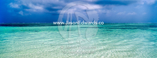 A tropical storm approaches the line of a reef on the horizon of calm turquoise seas. Bwejuu, Echo Beach Hotel, Echo Beach, Unguja Island, Zanzibar, Tanzania.