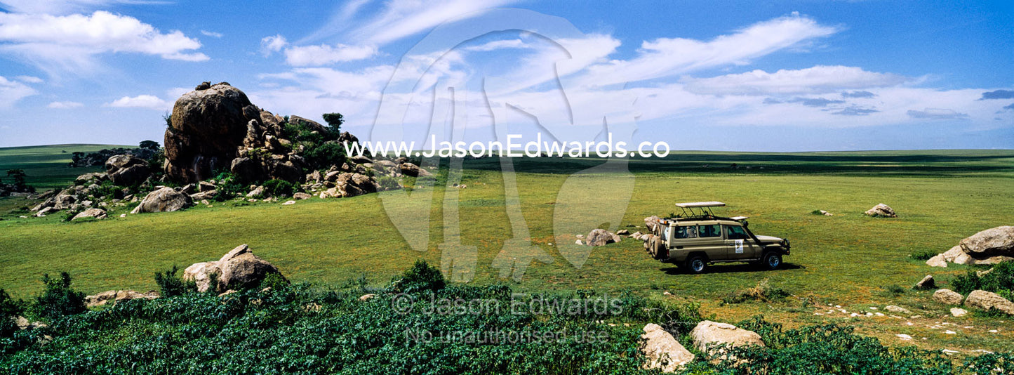 A safari 4WD beside rocky granite outcrop known as a kopje on a short grass savannah plain. Ngorongoro Conservation Area, Ngorongoro District, Tanzania.