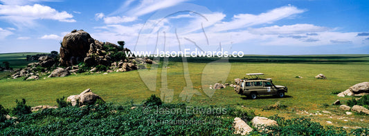 A safari 4WD beside rocky granite outcrop known as a kopje on a short grass savannah plain. Ngorongoro Conservation Area, Ngorongoro District, Tanzania.