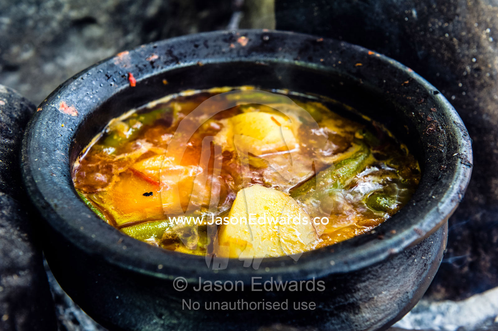 Traditional African food of potatoes, chilli and vegetables cooking in a handmade clay pot on a fire. Mto Wa Mbu, Lake Manyara National Park, Monduli District, Arusha Region, Tanzania.