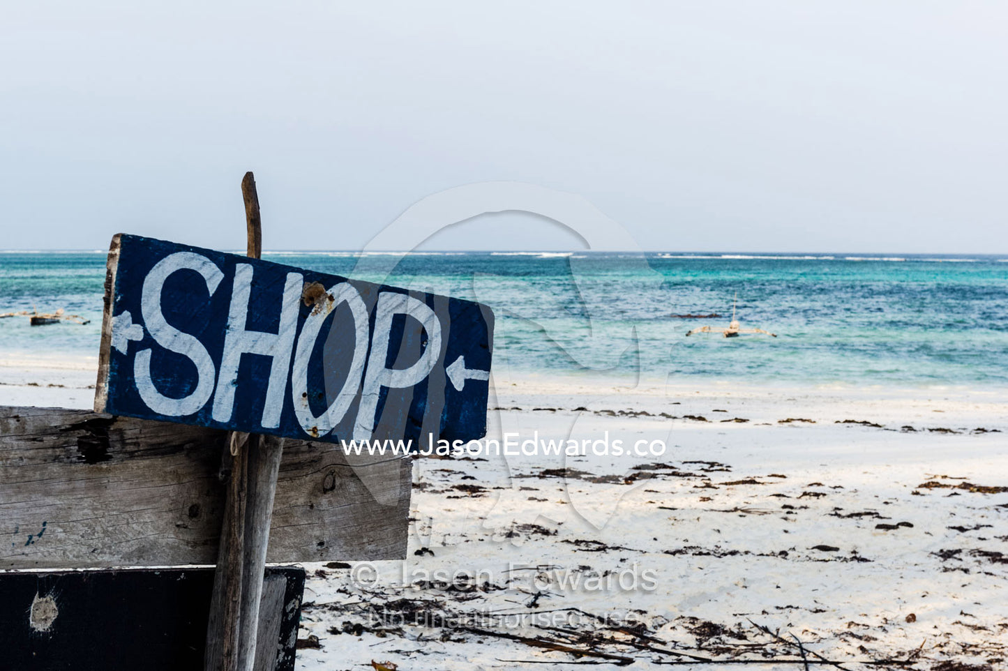 A hand-painted sign on a beach points to the local convenience store. Bwejuu, Unguja Island, Zanzibar, Tanzania.