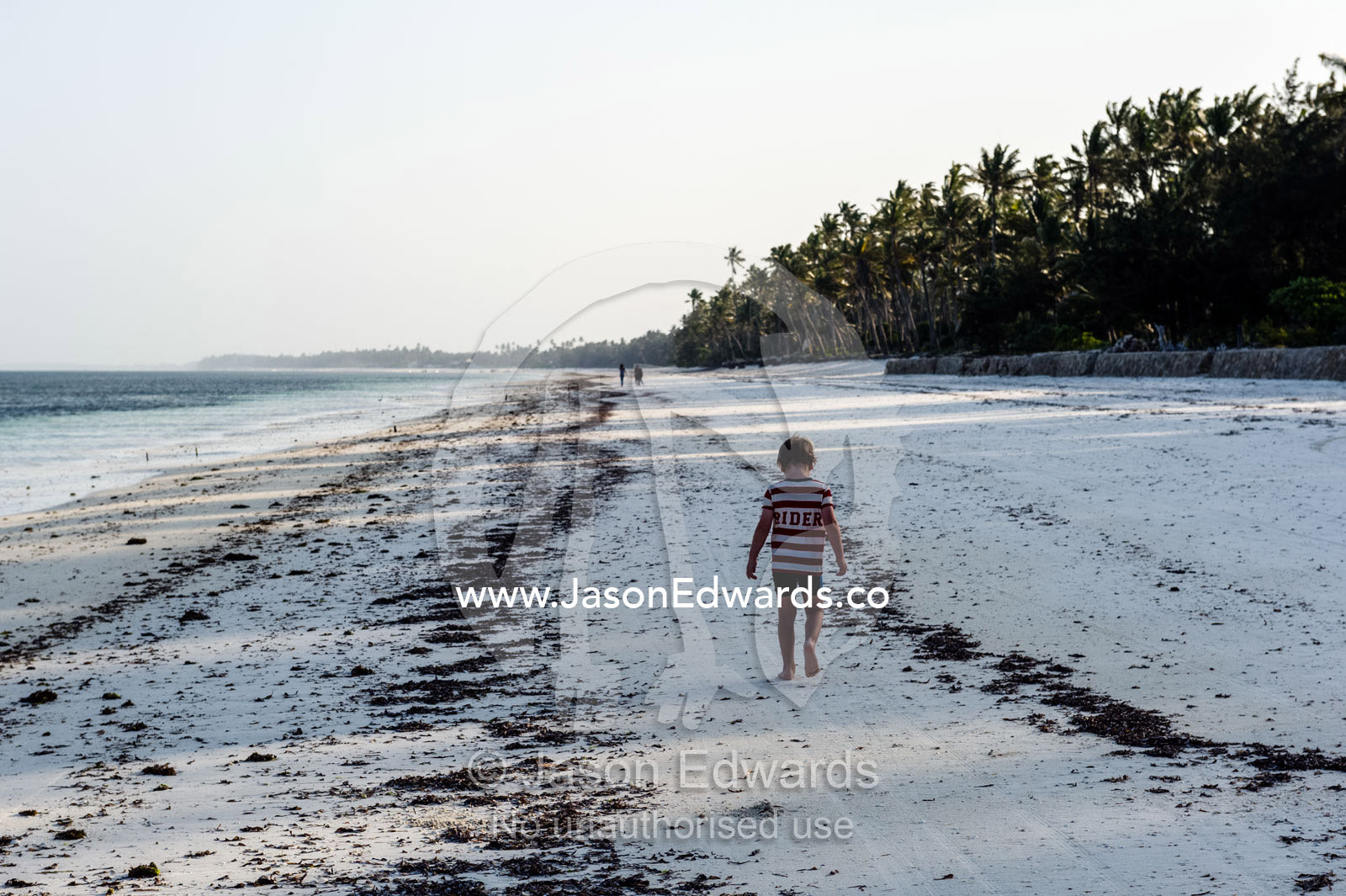 A small boy walking along a deserted tropical beach at sunset. Bwejuu, Echo Beach Hotel, Echo Beach, Unguja Island, Zanzibar, Tanzania.
