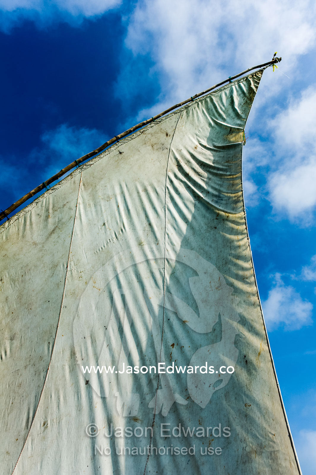 The tarpaulin sail and mast of a wooden dhow flapping in the breeze. Bwejuu, Unguja Island, Zanzibar, Tanzania.