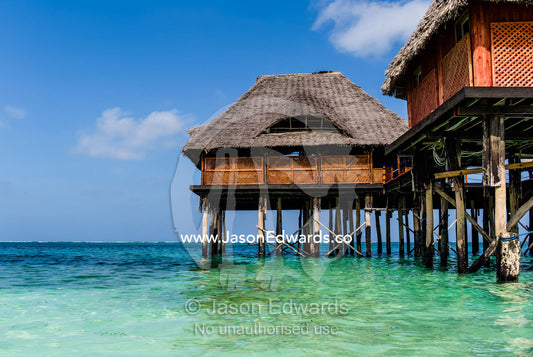Thatched huts on stilts overlooking the turquoise waters of the Indian Ocean. Bwejuu, Blue Lagoon Reef, Unguja Island, Zanzibar, Tanzania.