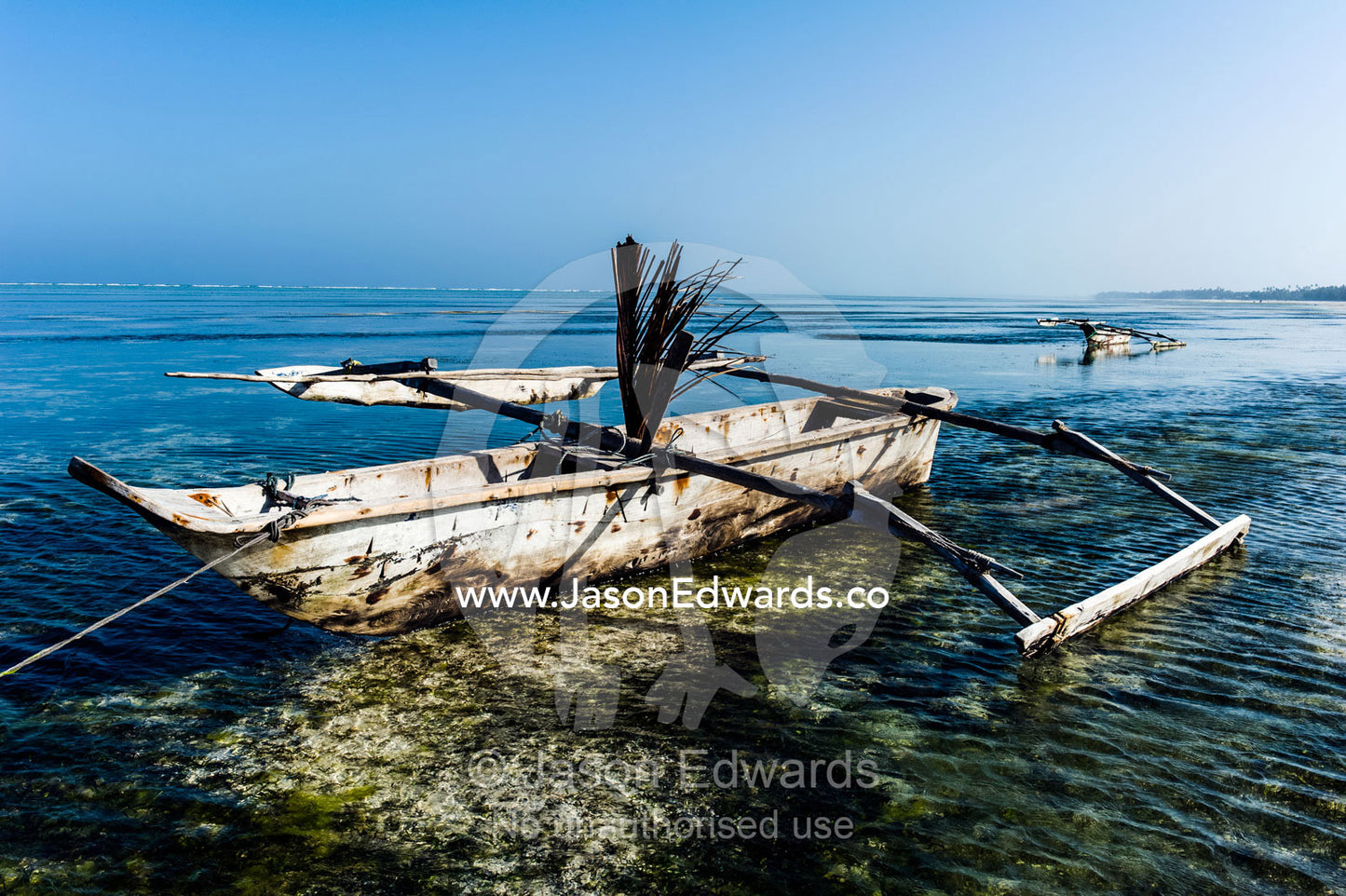 A wooden trimaran fishing dhow resting in the shallows of a tropical island at low tide. Bwejuu, Echo Beach Hotel, Echo Beach, Unguja Island, Zanzibar, Tanzania.