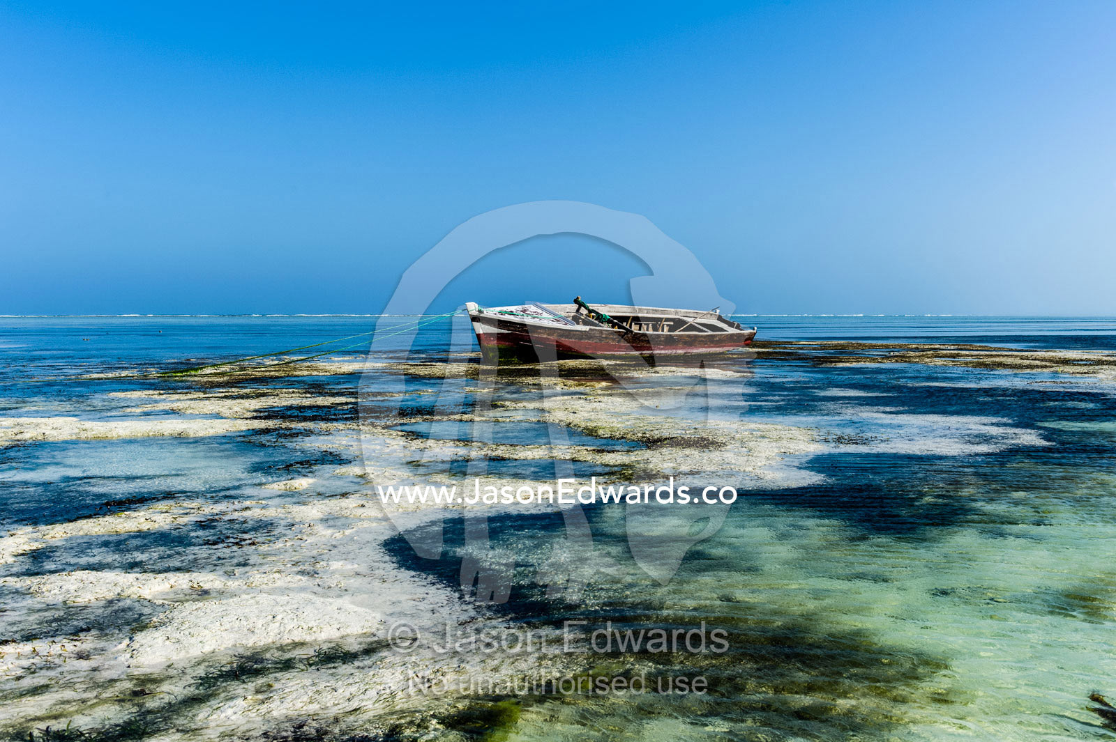 A wooden fishing boat resting in the shallows of a tropical island at low tide. Bwejuu, Echo Beach Hotel, Echo Beach, Unguja Island, Zanzibar, Tanzania.