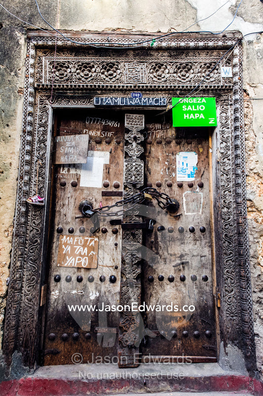 An ancient and weathered door featuring carvings is locked with a heavy chain. Stone Town, Mji Mkongwe, Zanzibar, Unguja Island, Zanzibar, Tanzania.