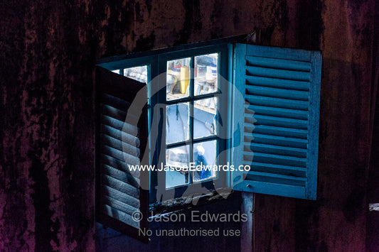 Looking through a shuttered window into the kitchen of a home in a trading port at night. Stone Town, Mji Mkongwe, Zanzibar, Unguja Island, Zanzibar, Tanzania.