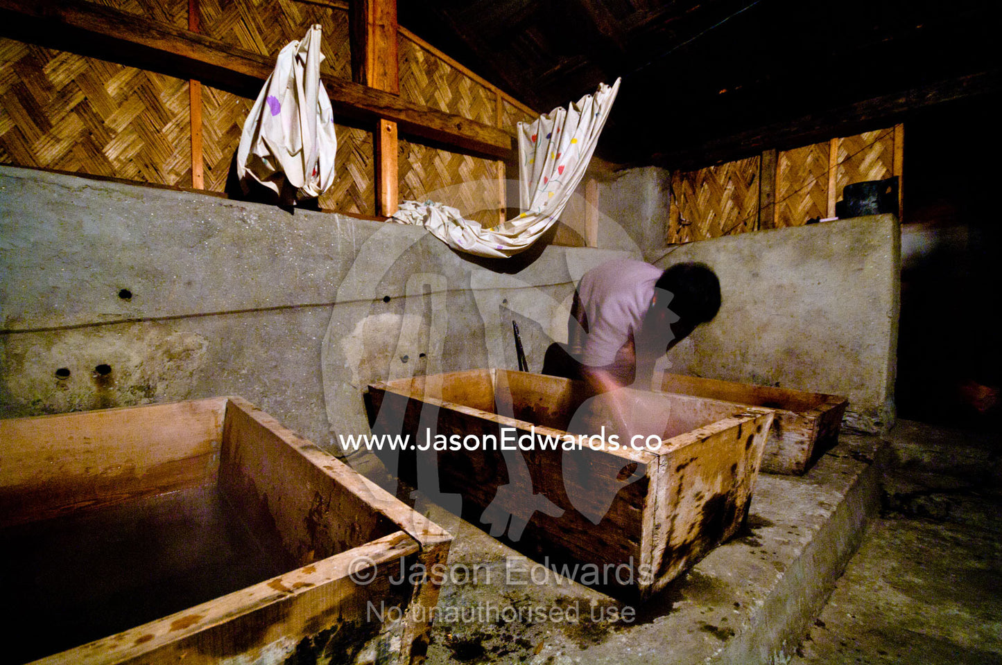 The wife of a farmer in a Himalaya village loads river rocks heated on a fire into timber baths for soaking. Thimphu, Thimphu District, Bhutan.