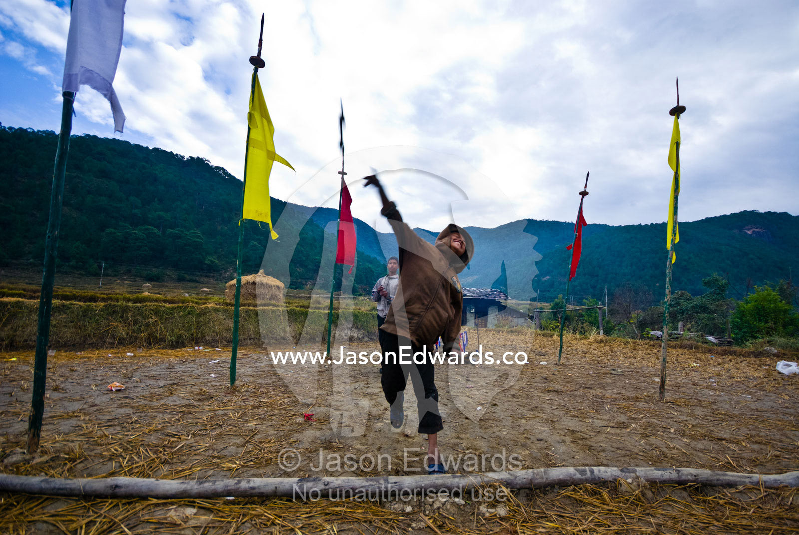 A village boy throws a large wooden dart known as khuru that is played during festivals. Punakha River, Punakha Valley, Punakha-Wangdiphodrang District, Bhutan.