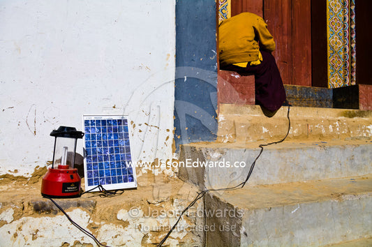 A Buddhist monk in a monastery attempts to fix a solar panel to charge his cell phone and camping lamp. Gangteng Monastery, Ganteng, Wangdue Phodrang District, Phobjika Valley, Phobjikha Valley, Gangteng Valley, Black Mountains, Bhutan.