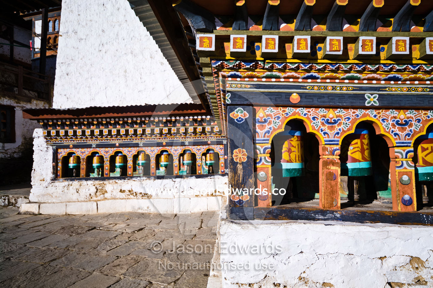 Colorful prayer wheels and painted facades along the wall of an ancient Buddhist monastery. Cheri Monastery, Chagri Dorjeden Monastery, Thimphu, Thimphu District, Bhutan.