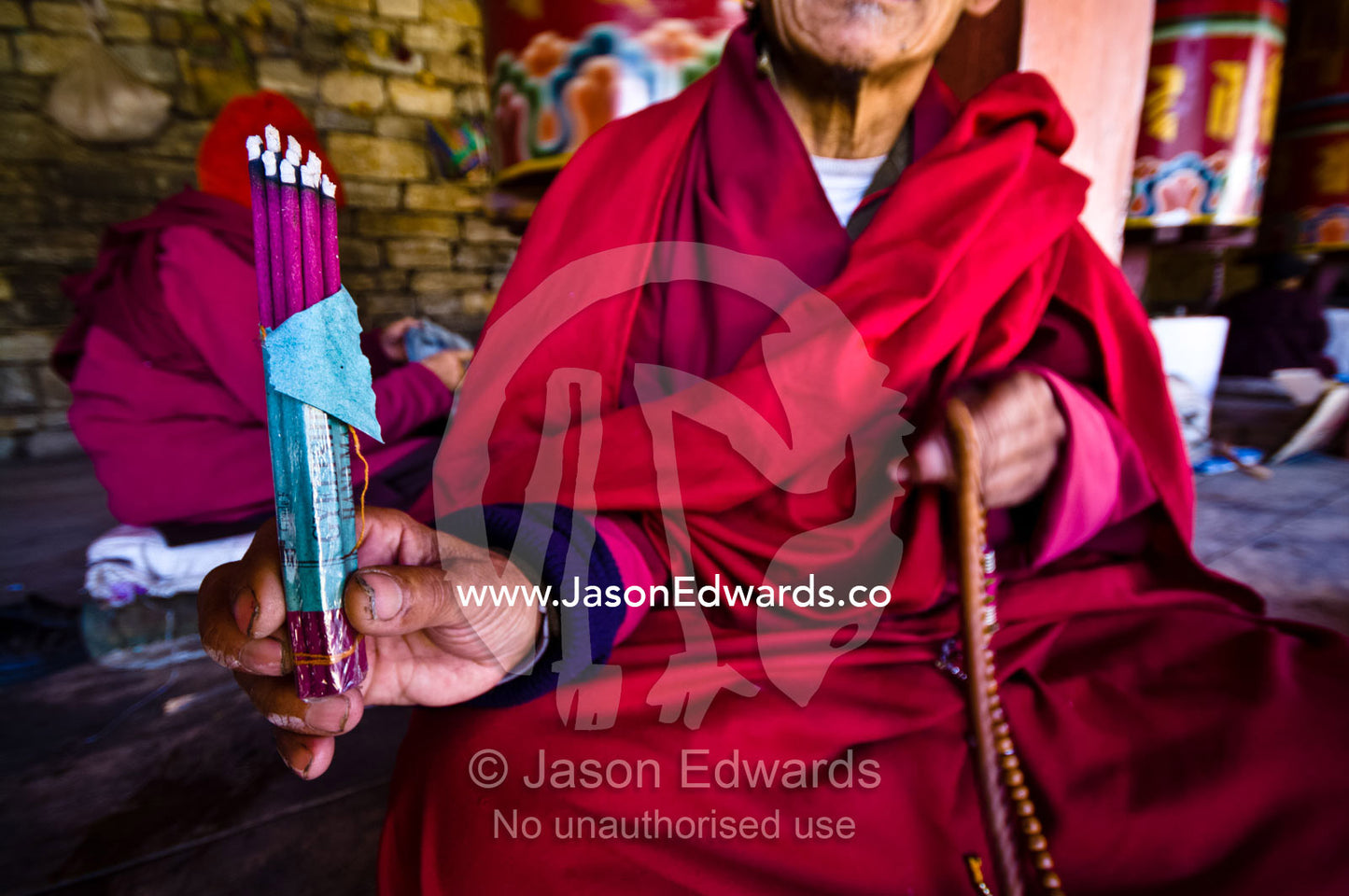 A Buddhist in red robes displays burning dhoop whilst seated beside prayer wheels at the Memorial Chorten. Thimphu Memorial Chorten, Thimphu Bhutan.