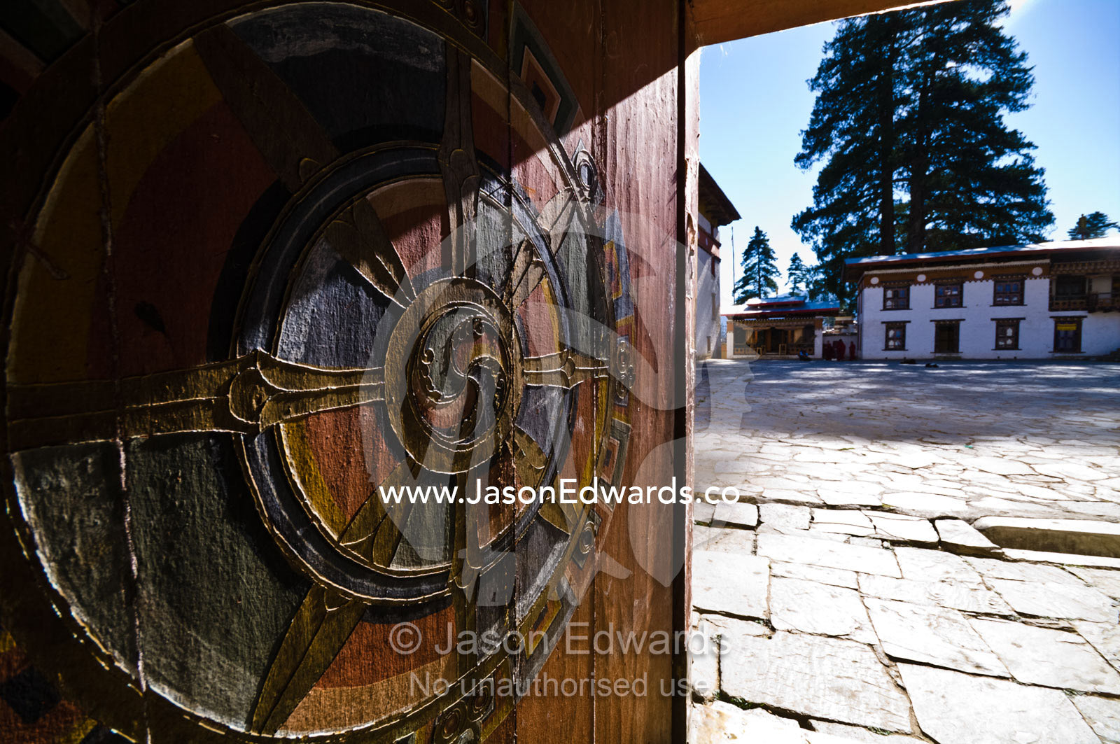 Dharmachakra carvings on a timber door leading to a paved courtyard in an Astrology school in the Himalaya. Pangri Zampa Astrology School, Thimphu, Thimphu District, Bhutan.