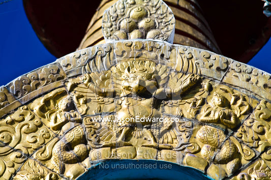 A golden Garuda on an arch beneath a golden spire and bells which reflect the bright sun. Thimphu Memorial Chorten, Thimphu Bhutan.