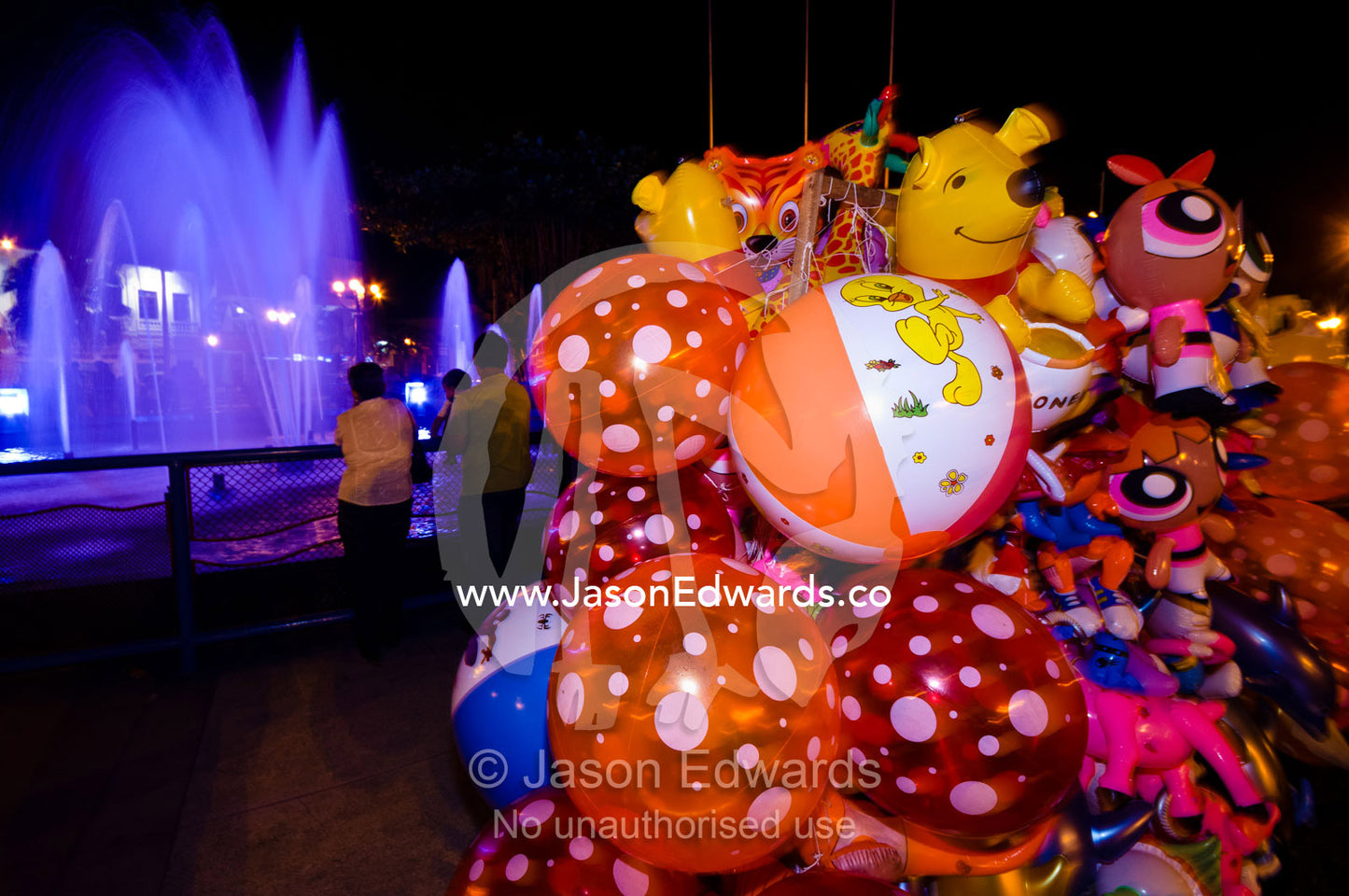Traders sell balloons as tourists take a night time stroll to watch the fountain in a local square. Plaza de Armas, Iquitos, Amazon Basin, Loreto Region, Maynas Province, Peru.