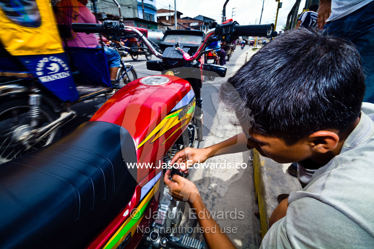 An auto rickshaw driver does makeshift repairs to his motorbike on a busy street. Puerto Masusa, Iquitos, Amazon Basin, Loreto Region, Maynas Province, Peru.