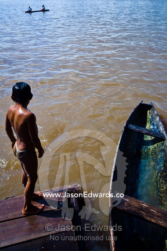 A young boy peers over the edge of jetty into the Amazon River, gauging his next jump. Iquitos, Rio Amazonas, Loreto Region, Maynas Province, Amazon Basin, Peru.