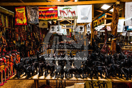 African Elephants, lions and other wildlife carved from mahogany timber for sale to tourists in a roadside stall. Maasai Mara National Reserve, Narok County, Kenya.