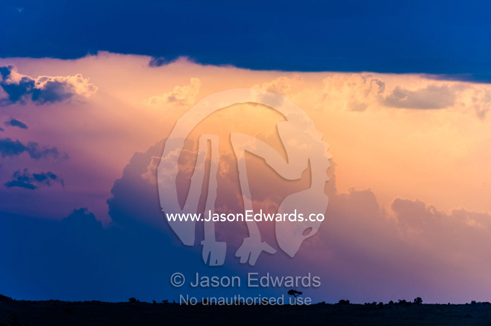 Pastel sunrays caress storm clouds descending into the horizon at sunset. Maasai Mara National Reserve, Narok County, Kenya.