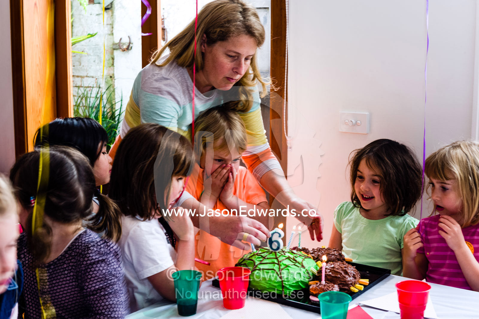 A boy blowing out the candles on his cake at his birthday party surrounded by his friends. Carlton North, Melbourne, Victoria, Australia.