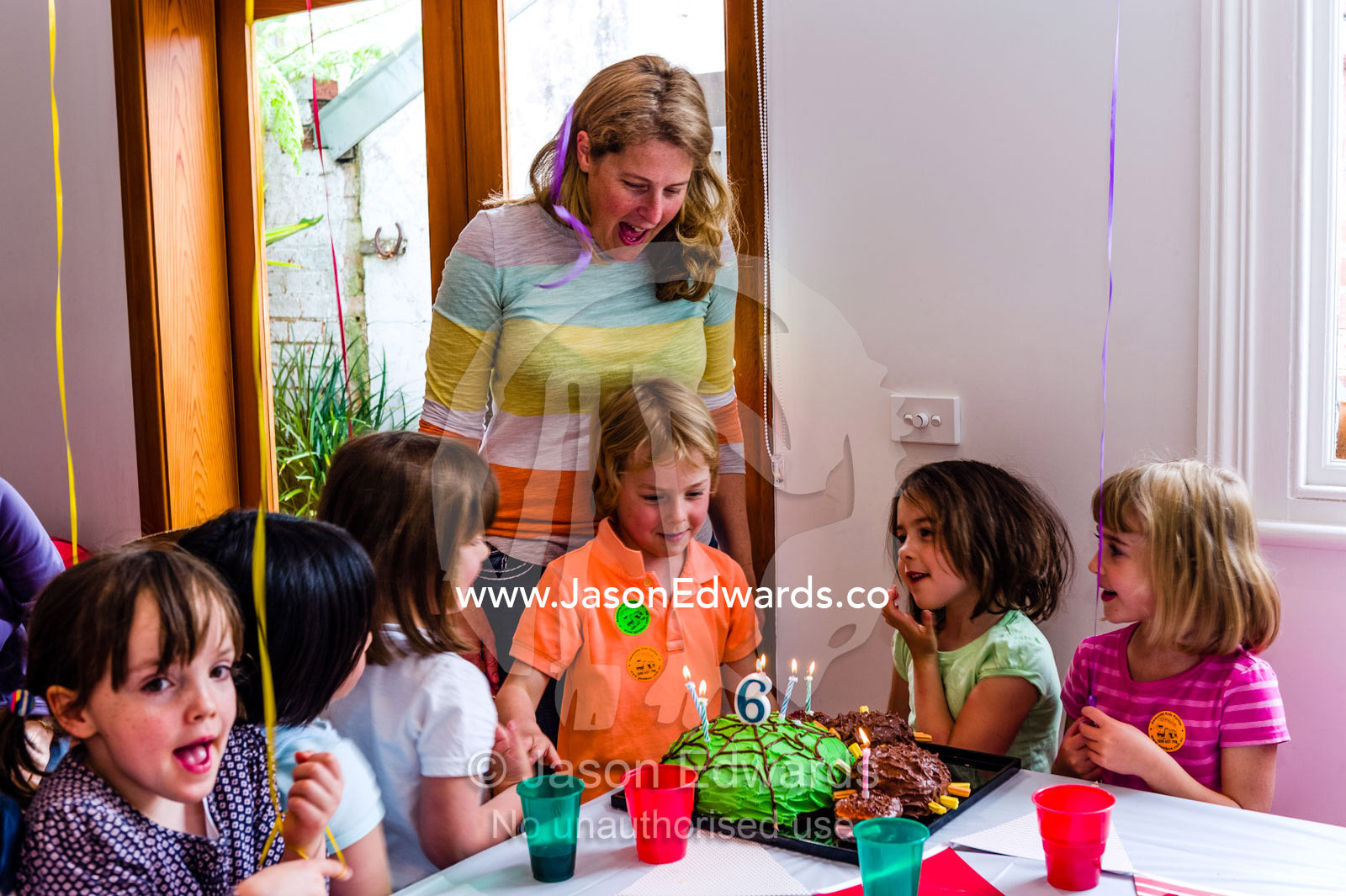 A boy blowing out the candles on his cake at his birthday party surrounded by his friends. Carlton North, Melbourne, Victoria, Australia.