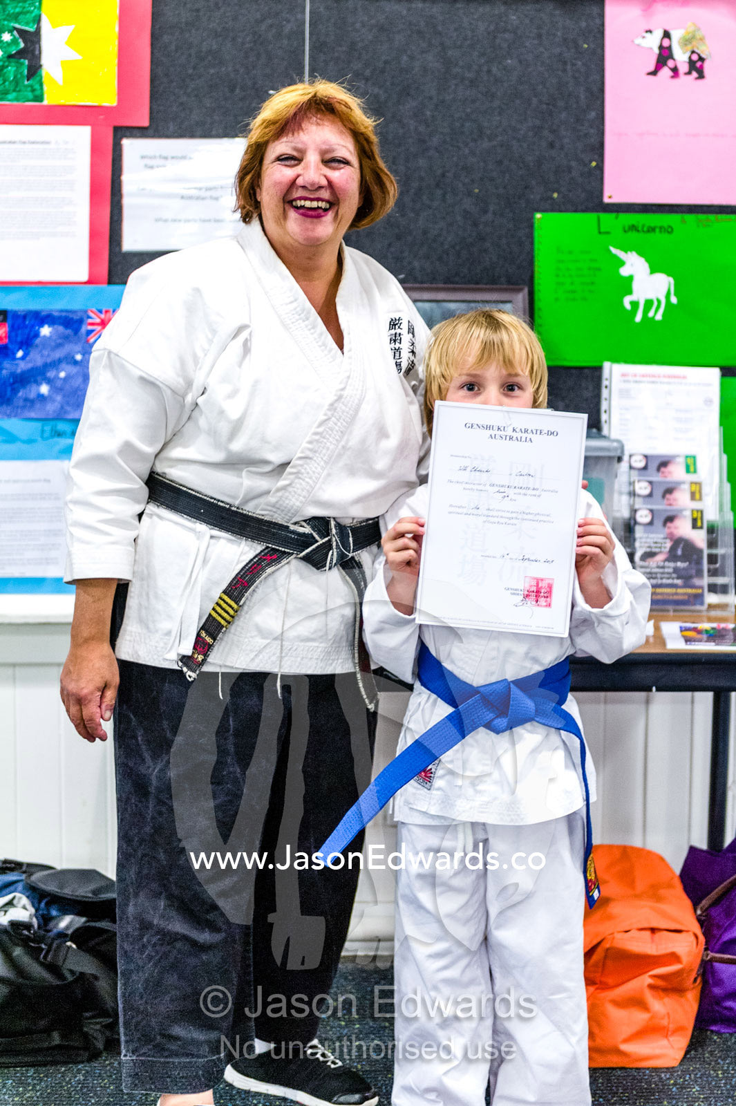 A karate instructor presents a young student with an award for obtaining a blue belt grading. Carlton North, Melbourne, Victoria, Australia.
