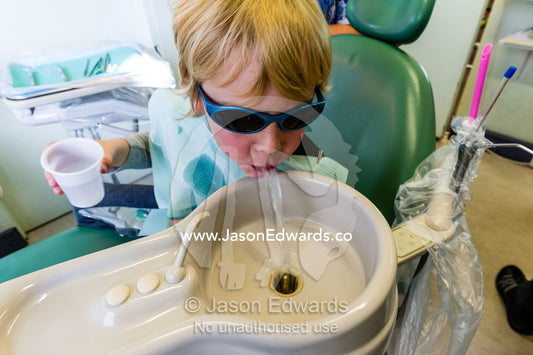 A boy rinses his mouth into a wash basin sink after treatment on his teeth by a dentist. East Melbourne, Melbourne, Victoria, Australia.
