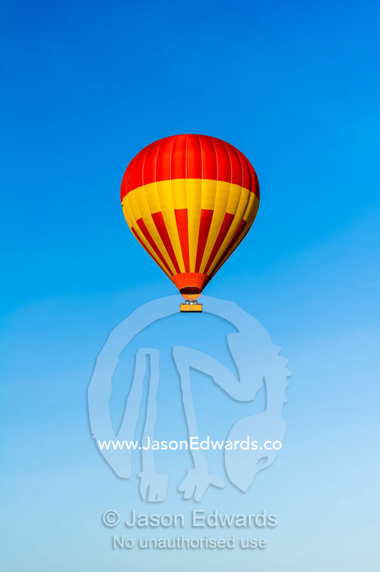 A hot air ballon floating in a clear blue sky above the African savannah. Maasai Mara National Reserve, Masai Mara, Narok County, Kenya.