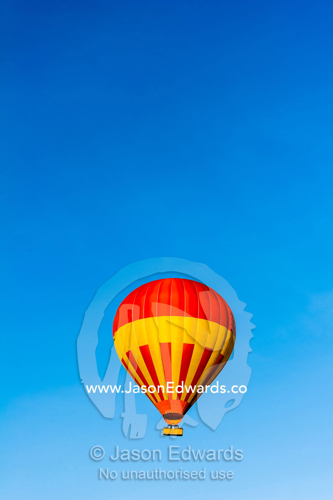 A hot air ballon floating in a clear blue sky above the African savannah. Maasai Mara National Reserve, Masai Mara, Narok County, Kenya.