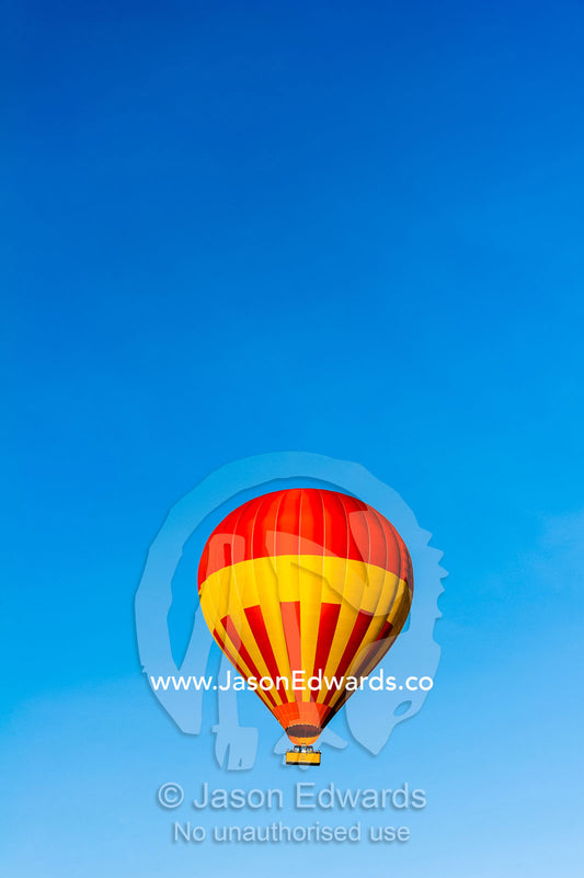 A hot air ballon floating in a clear blue sky above the African savannah. Maasai Mara National Reserve, Masai Mara, Narok County, Kenya.