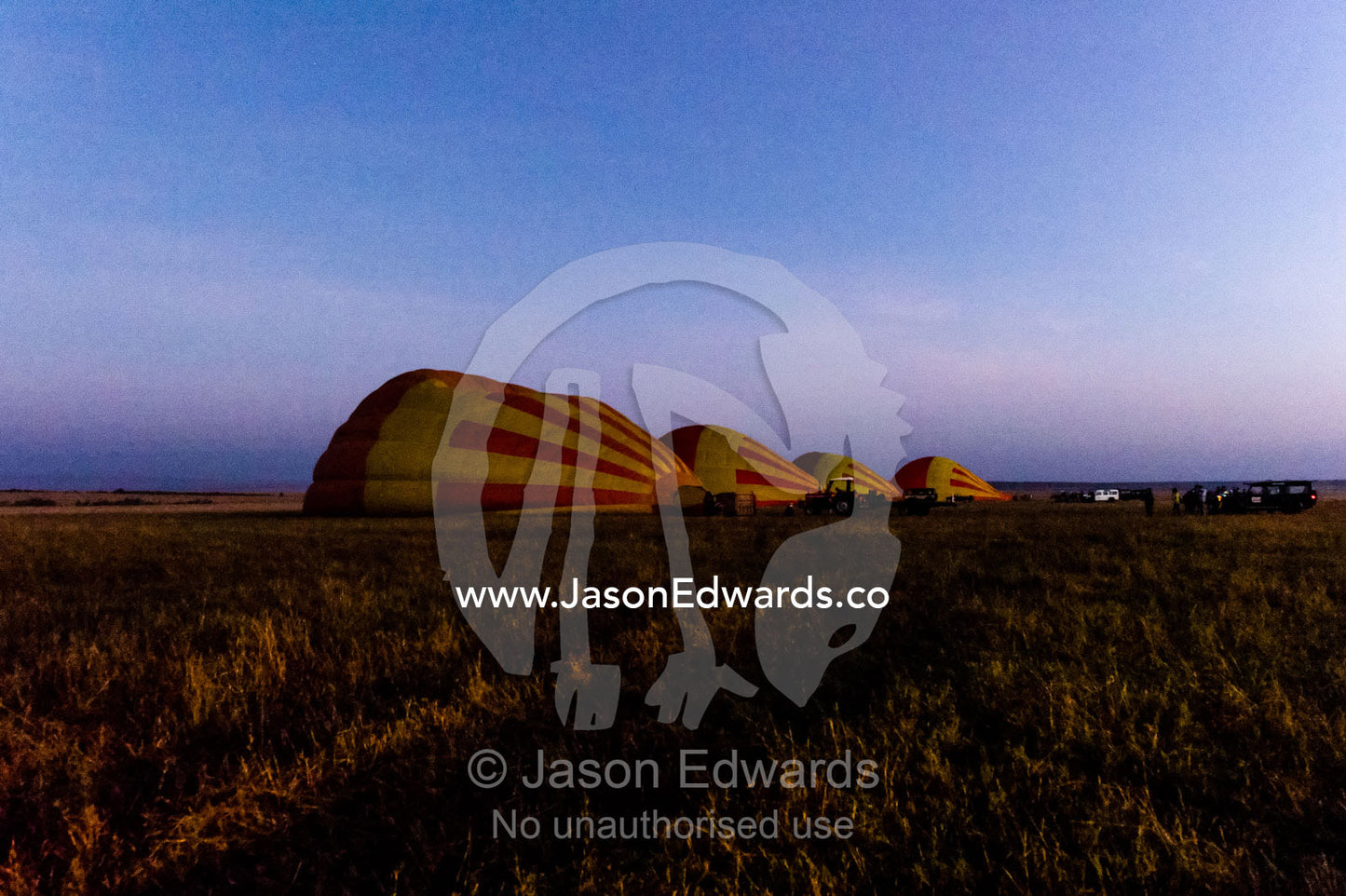 A row of hot air balloons on the African savannah waiting to be inflated for tourist flights. Maasai Mara National Reserve, Masai Mara, Narok County, Kenya.