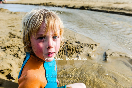 A boy playing in the sand beside a tidal stream flowing down a beach. Wye River, Great Ocean Road, Victoria, Australia.