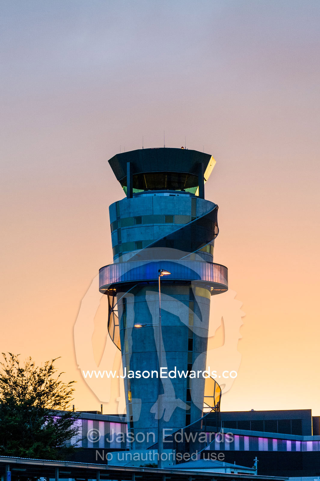 Neon lights illuminate a modern control tower that monitors flights over an airport at sunset Christchurch International Airport, Christchurch, South Island, New Zealand.