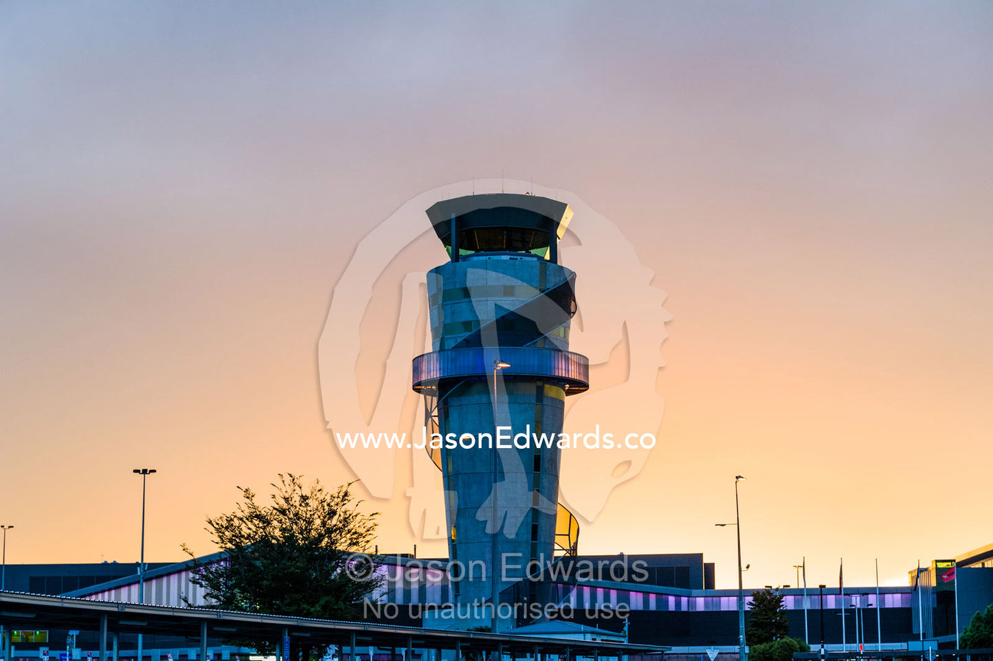 Neon lights illuminate a modern control tower that monitors flights over an airport at sunset. Christchurch International Airport, Christchurch, South Island, New Zealand.