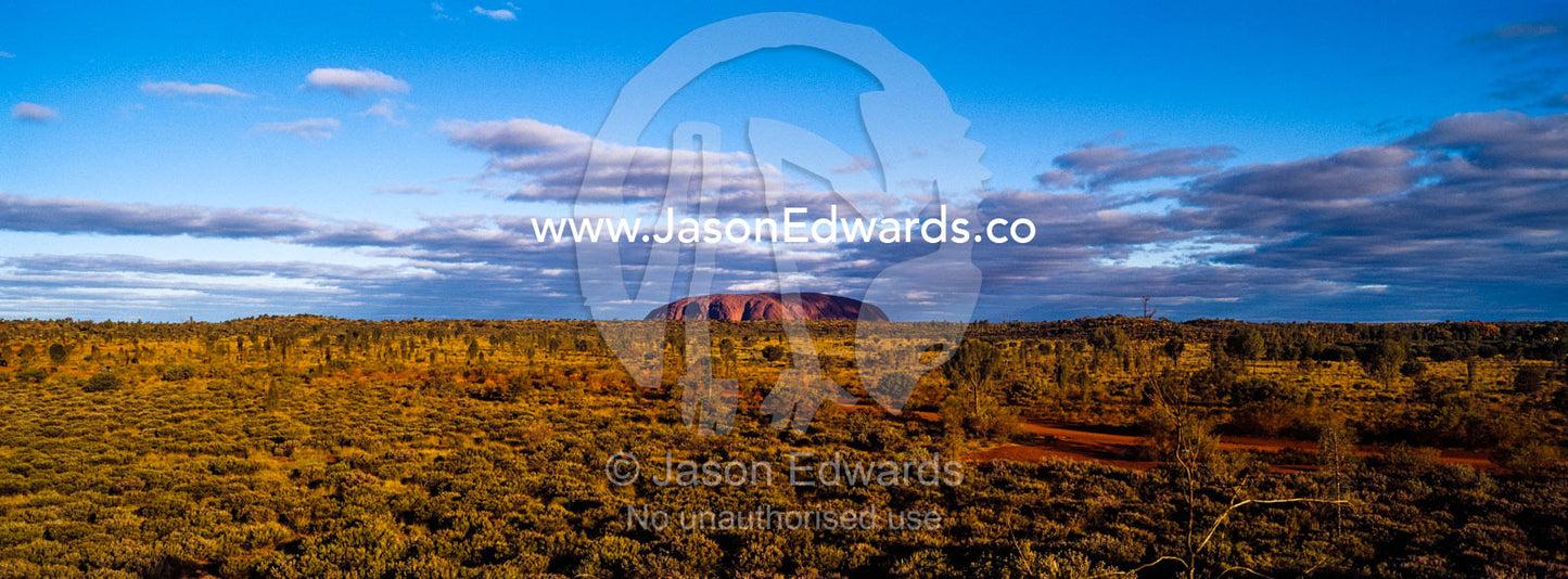 The vast desert plain of the Australian outback dwarfs the dome of Uluru on the horizon. Uluru Kata Tjuta National Park, Northern Territory, Australia.