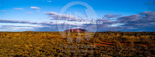 The vast desert plain of the Australian outback dwarfs the dome of Uluru on the horizon. Uluru Kata Tjuta National Park, Northern Territory, Australia.