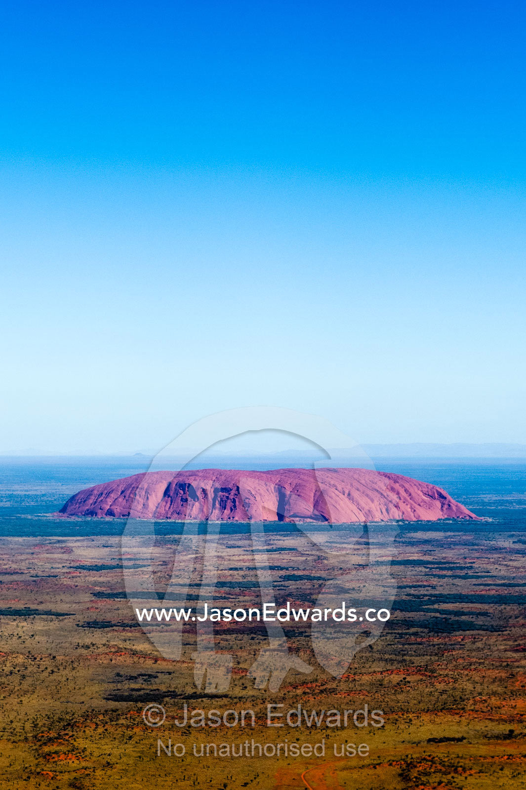 The ochre sandstone dome of Uluru rises from a vast desert plain in Australia's Outback. Uluru Kata Tjuta National Park, Northern Territory, Australia.