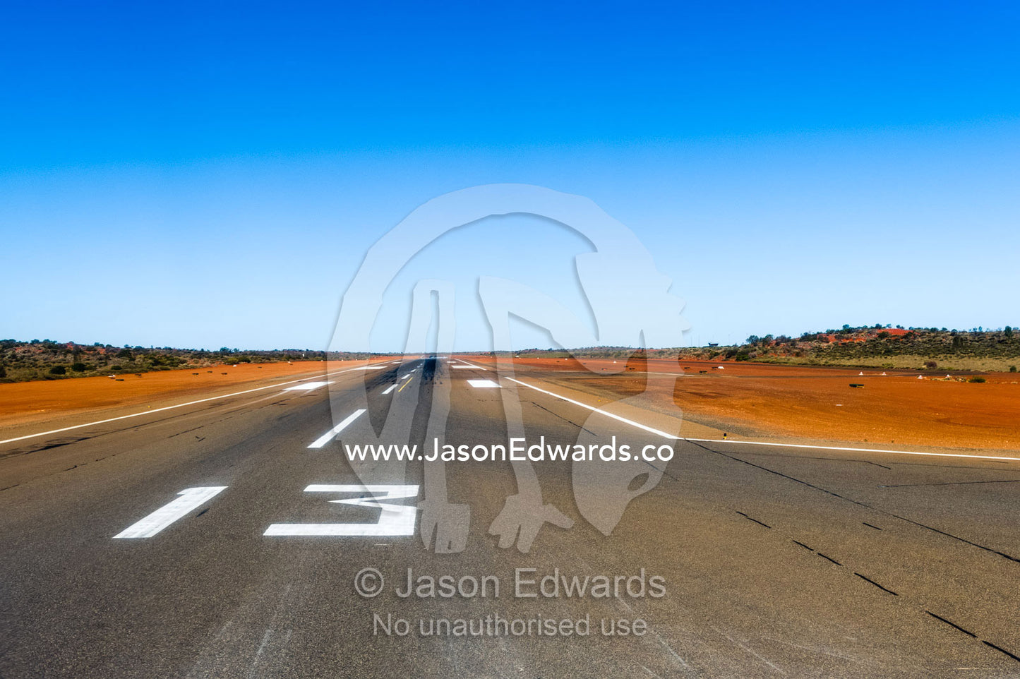 An airport runway stretches across the red sand of the Australian outback. Uluru Kata Tjuta National Park, Northern Territory, Australia.
