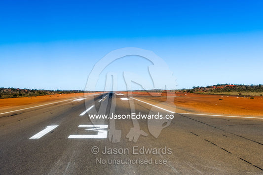 An airport runway stretches across the red sand of the Australian outback. Uluru Kata Tjuta National Park, Northern Territory, Australia.