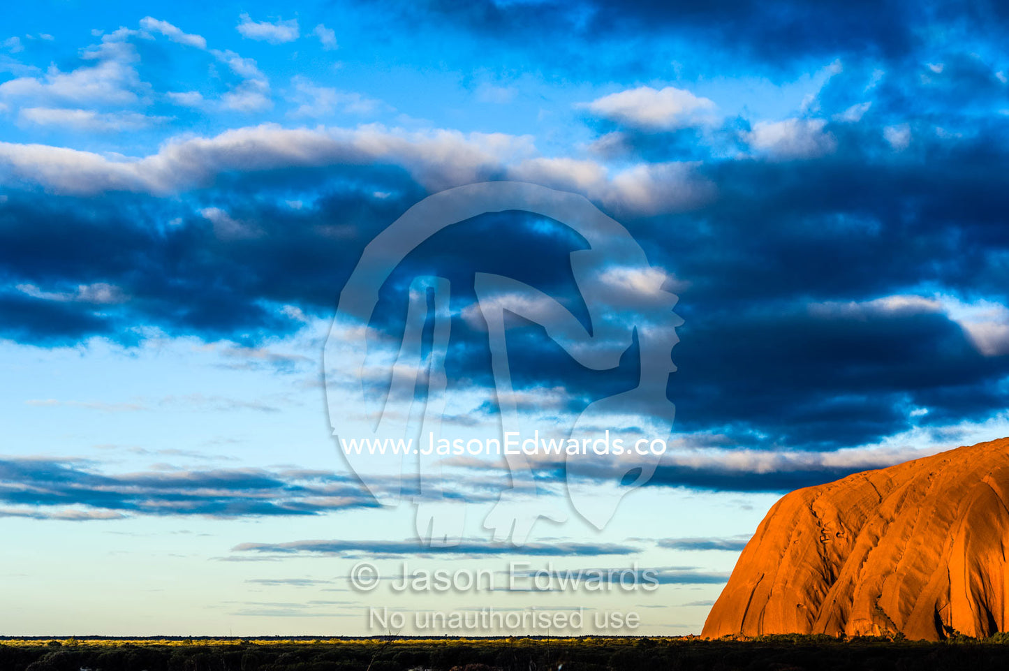 The last sunrays of sunset touch the sandstone massive of Uluru on the desert plain. Uluru Kata Tjuta National Park, Northern Territory, Australia.