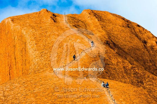 Uluru dwarfs tourists and walkers using a chain to climb its steep, smooth, oxidized slopes. Uluru Kata Tjuta National Park, Northern Territory, Australia.