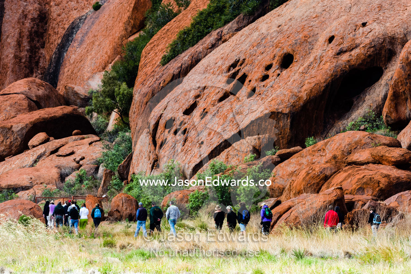 Tourists hike around the base of Uluru with a guide to learn about its geology and history. Uluru Kata Tjuta National Park, Northern Territory, Australia.