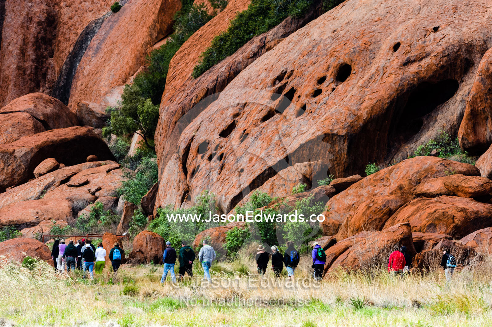 Tourists hike around the base of Uluru with a guide to learn about its geology and history. Uluru Kata Tjuta National Park, Northern Territory, Australia.