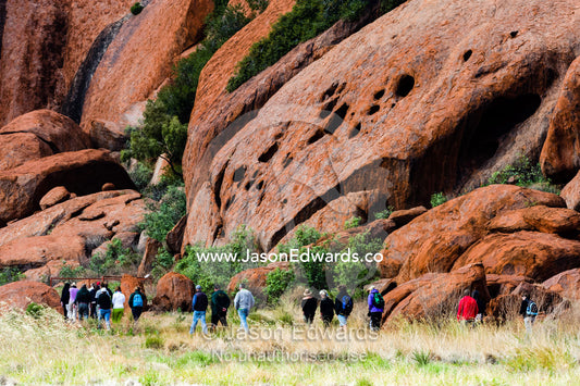 Tourists hike around the base of Uluru with a guide to learn about its geology and history. Uluru Kata Tjuta National Park, Northern Territory, Australia.